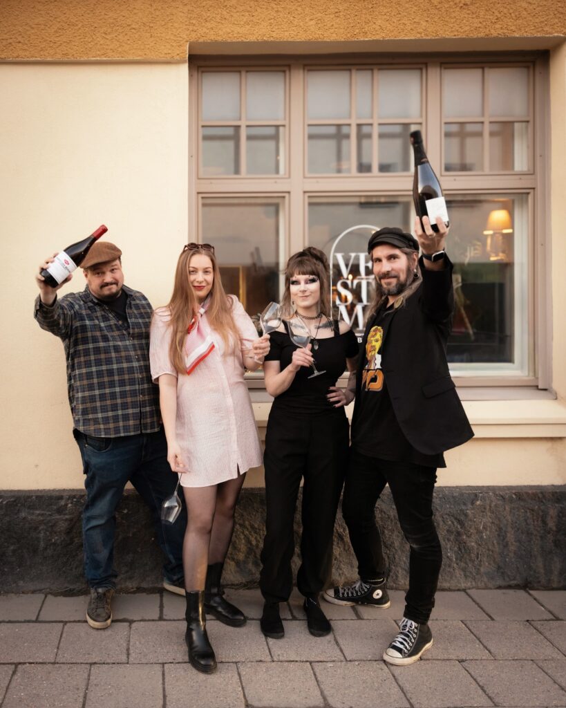 Neljä  henkilöä iloitsevat käsissään viinipullot ja viinilasit.