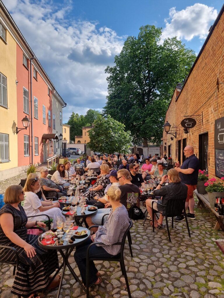Aurinkoinen mukulakivikatu täynnä ihmisiä.